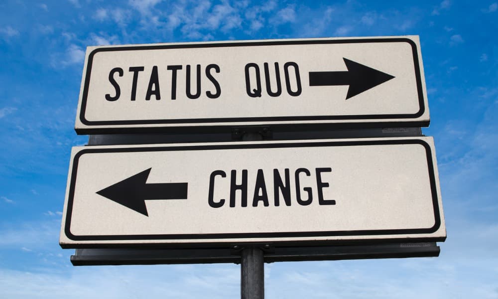 A road sign has arrows pointing in two directions. One says status quo, and the other reads change.