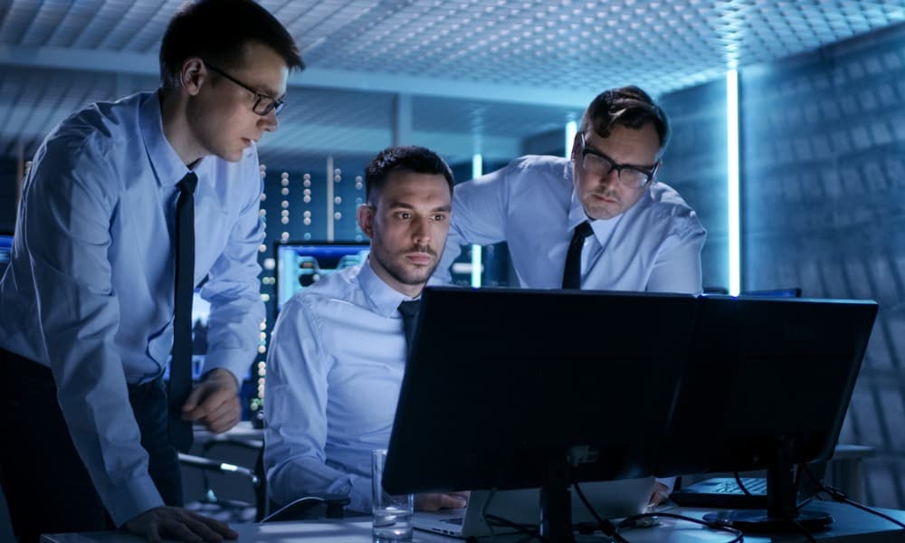 Three IT engineers huddle around a computer screen to solve an issue remotely.