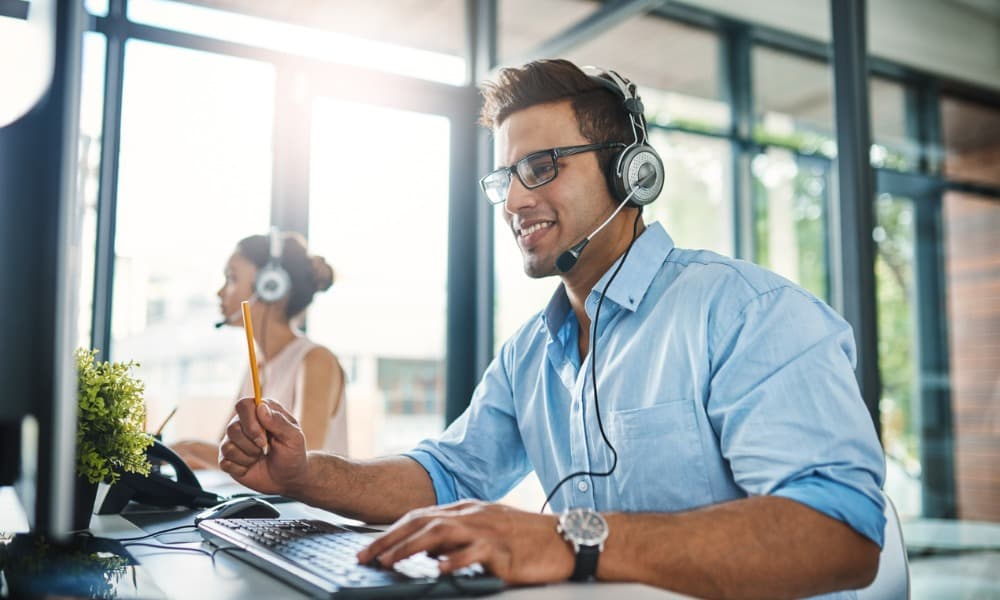 A young male employee of an IT managed services provider takes a client call for help desk service. 